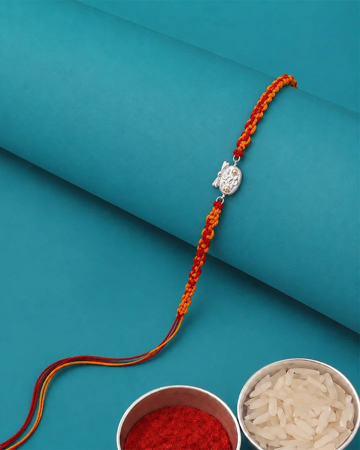 An orange and red braided Rakhi with a silver-toned owl charm.