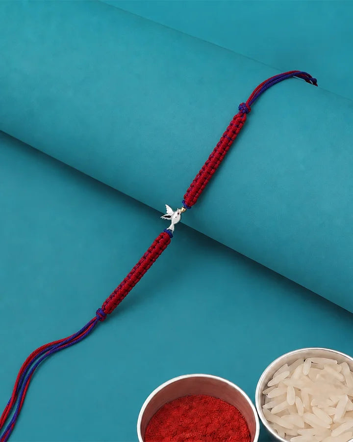 A red braided Rakhi bracelet with a silver-colored swastika symbol charm.