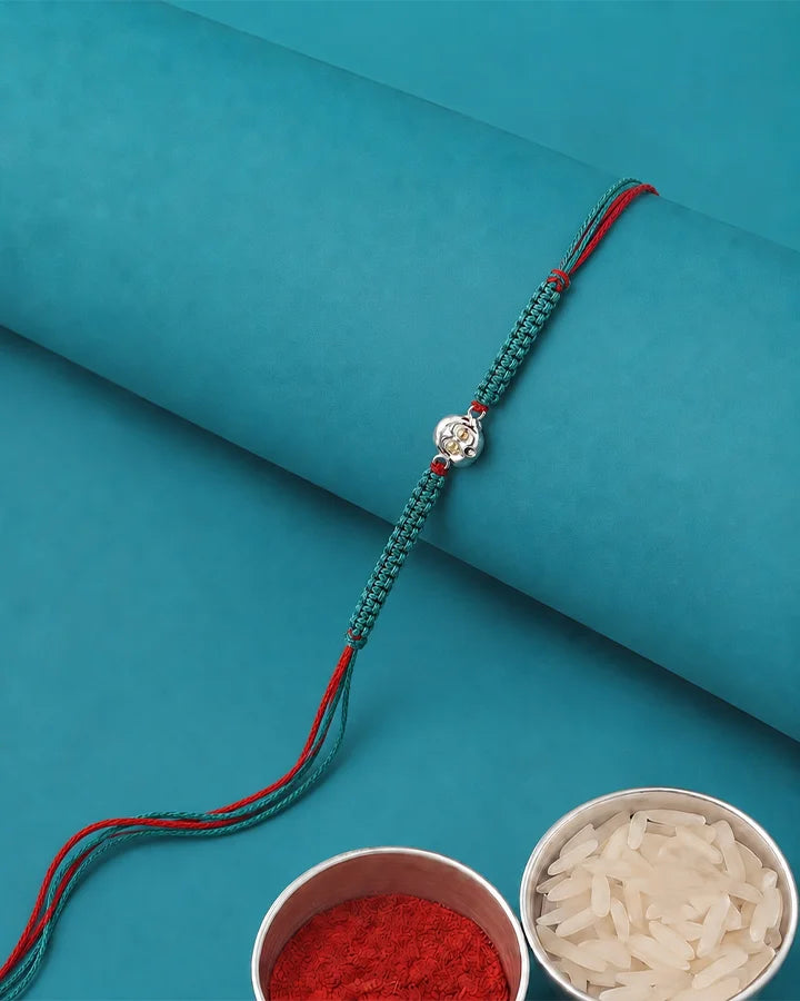 A teal and red braided string bracelet with a silver-toned decorative charm