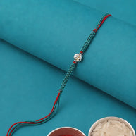A teal and red braided string bracelet with a silver-toned decorative charm