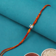 A braided Rakhi with red and orange threads and a silver cow pendant