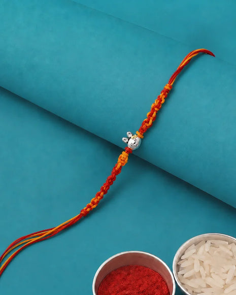 A braided Rakhi with red and orange threads and a silver cow pendant